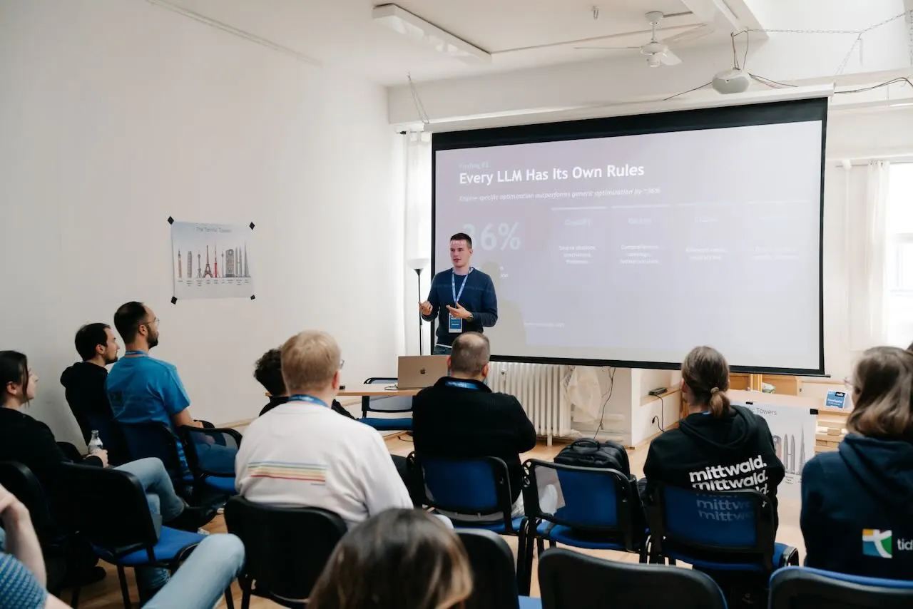 Alex Jank giving his “Beyond SEO” talk at SCUC 2026 in Cologne — the screen shows a slide about each LLM’s own ranking rules