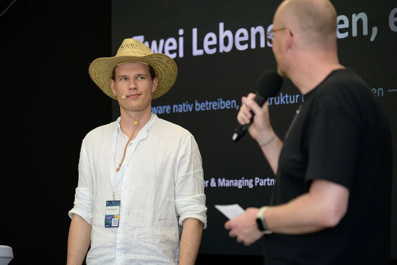 Alex Jank auf der Bühne der mittwald Head in the Cloud 2026 in Espelkamp im Gespräch mit dem Moderator
