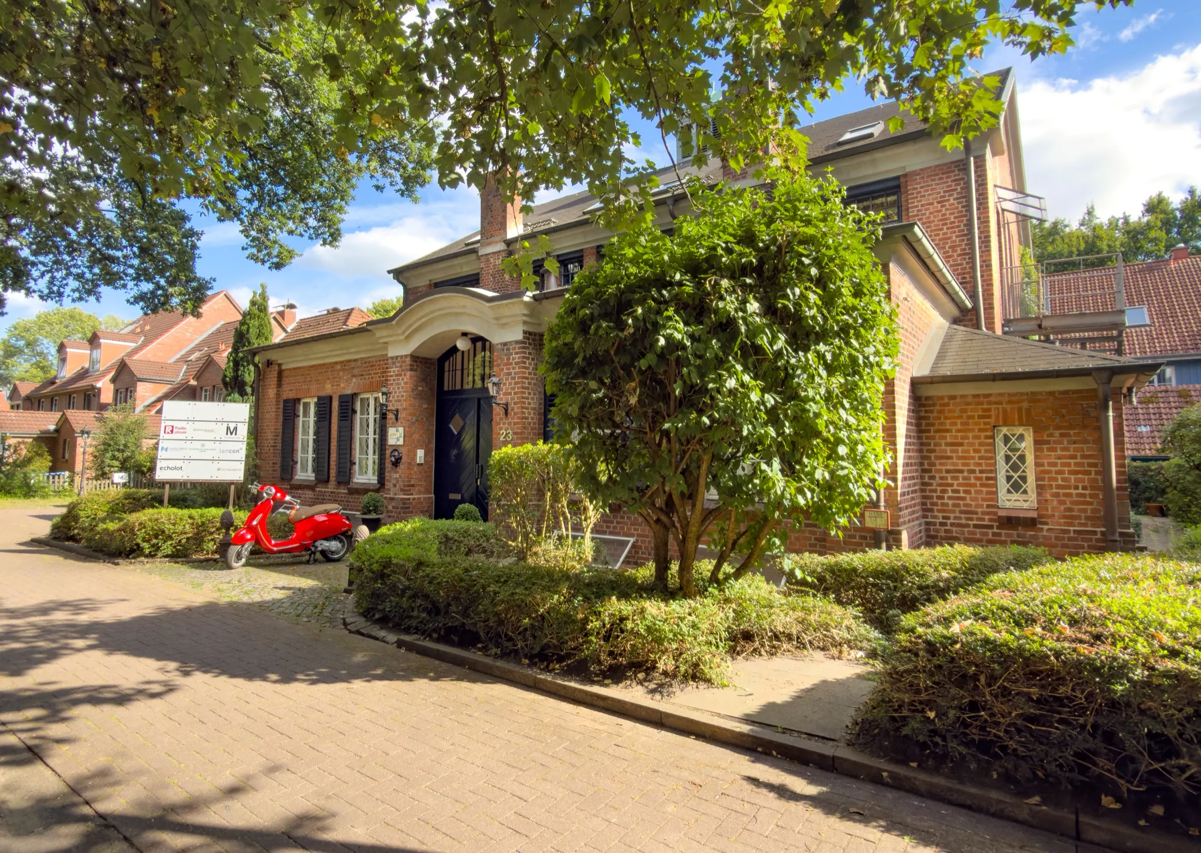 Backstein-Kontorhaus Bei der Pulvermühle 23 in Hamburg-Niendorf, der Sitz des nuonic-Büros, mit begrüntem Vorplatz und roter Vespa vor dem Eingang